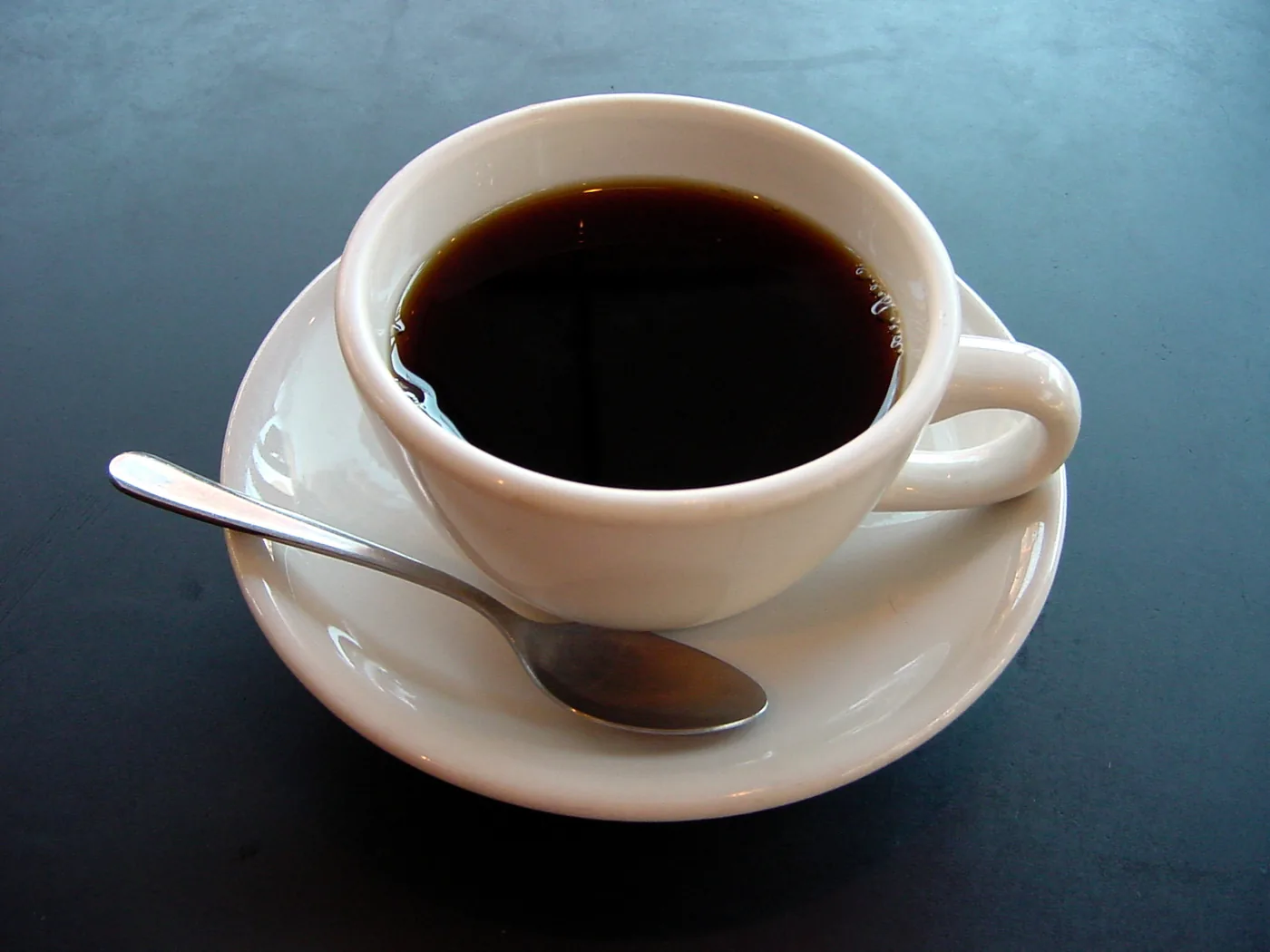 A cup of black coffee on a saucer with a spoon