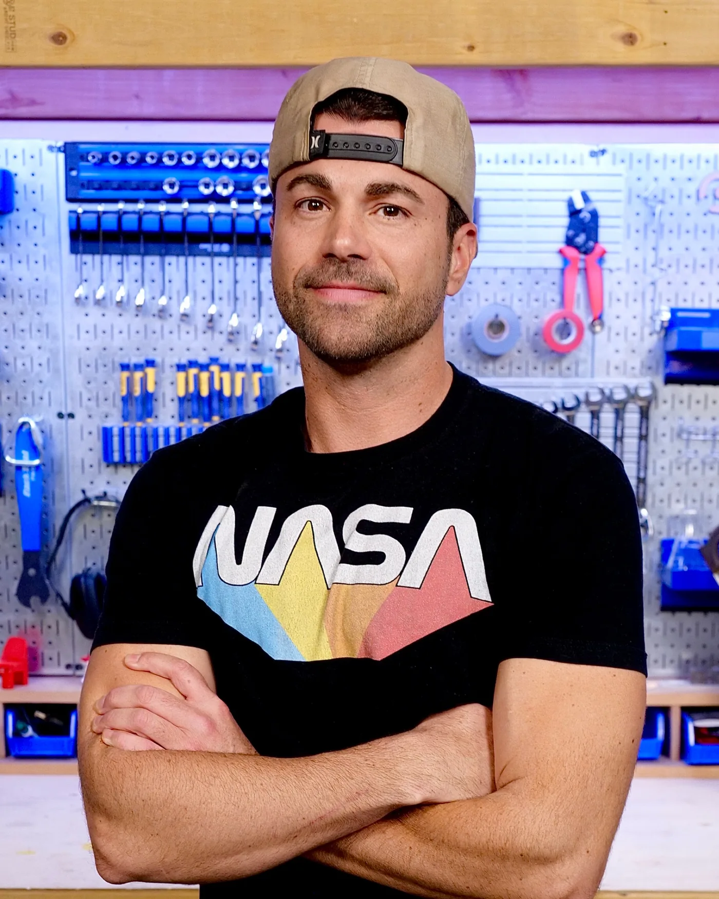 Mark Rober in a NASA T-shirt in front of a pegboard of tools in his workshop