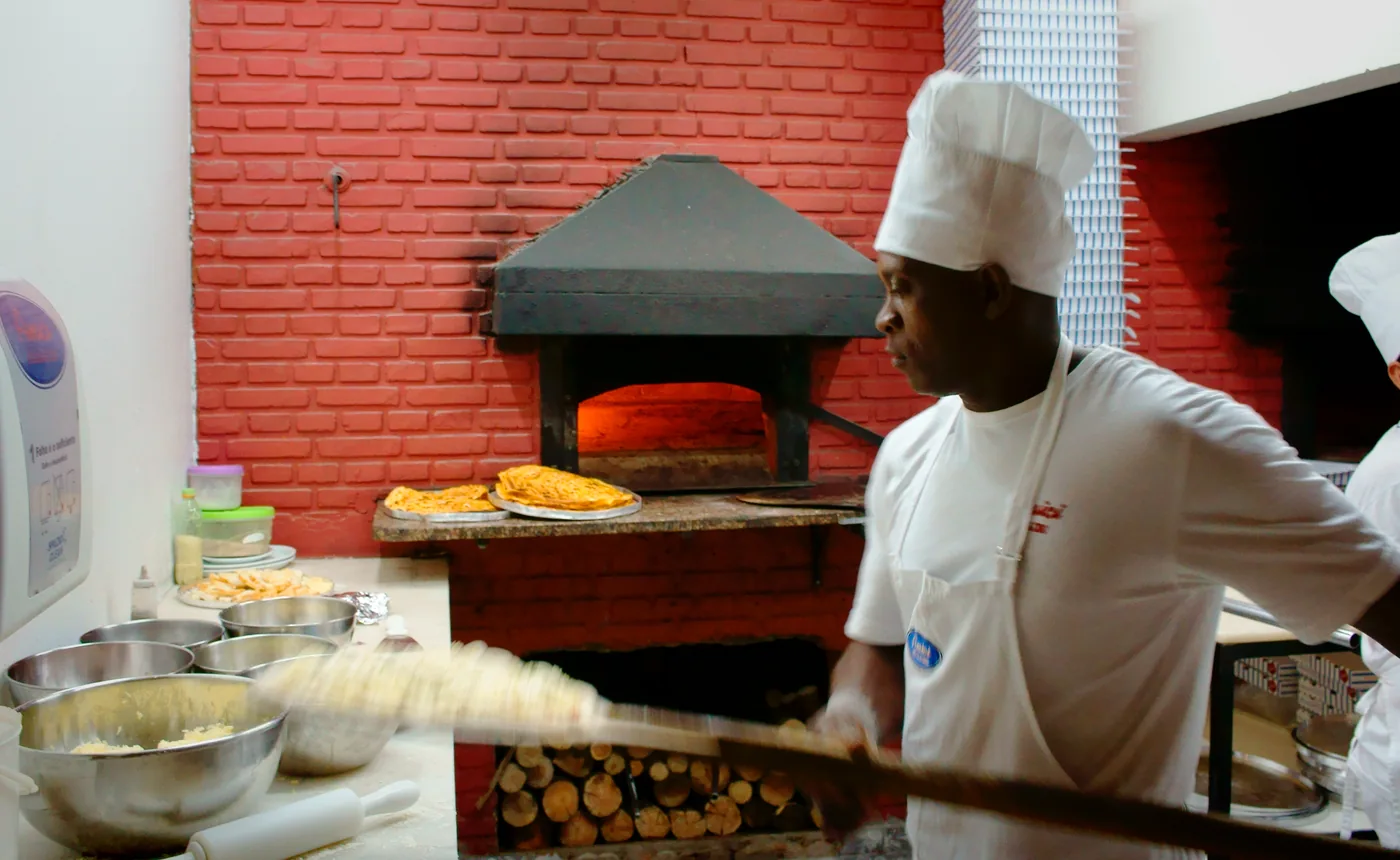 A pizzaiolo sliding a pizza into a wood-fired oven