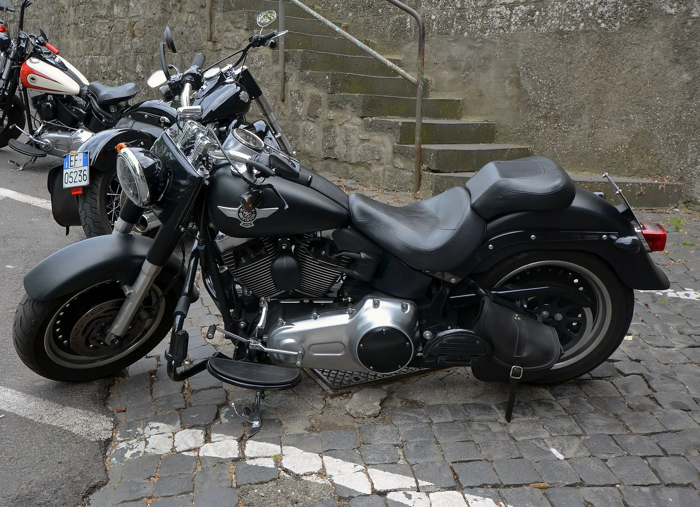 A matte-black Harley-Davidson Fat Boy parked on cobblestones